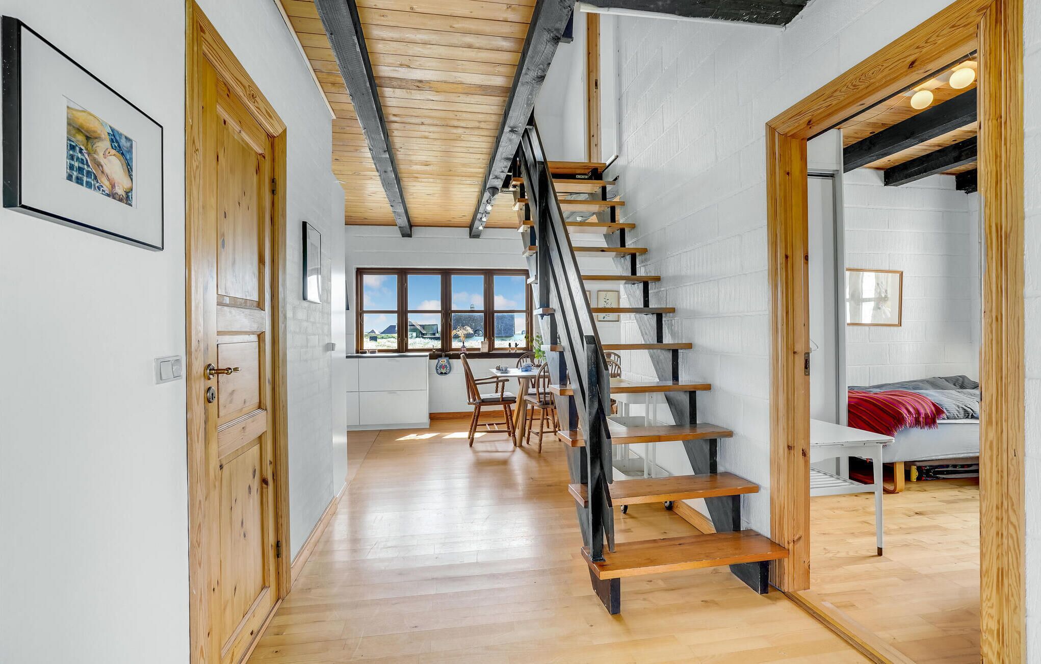 A modern interior with a wooden staircase, a dining area, and a view through large windows.