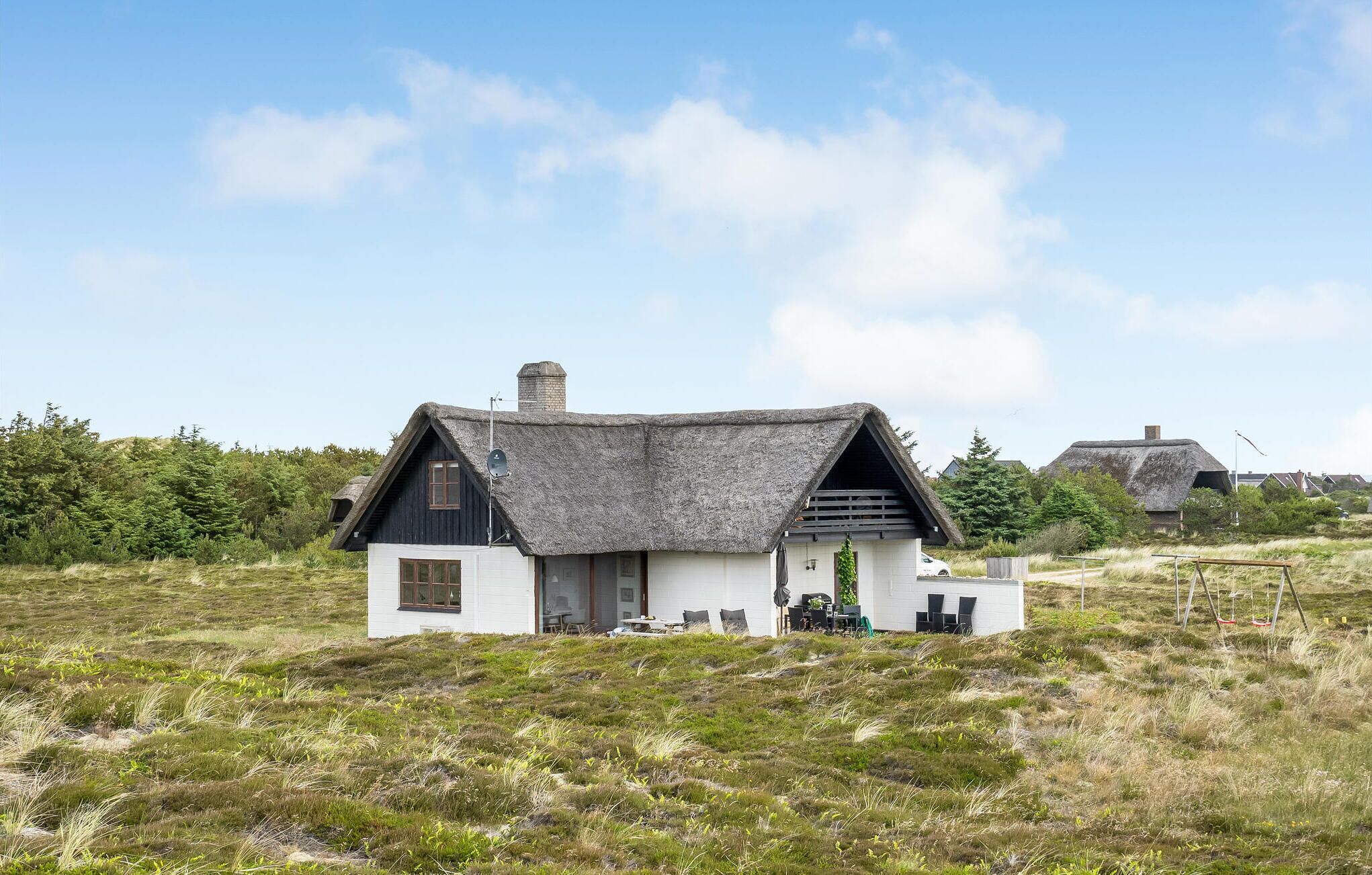 A white house with a thatched roof, a chimney, and a small porch with outdoor seating.