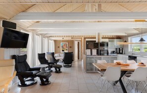 Et moderne interiør med spiseplads, køkken og siddeområde med et fjernsyn ophængt på væggen.
