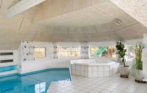 Ein großes Hallenbad mit Whirlpool, gefliesten Wänden und großen Fenstern.