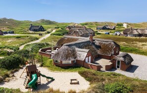 En bygning med stråtækt tag, et sandareal og en grøn rutchebane i nærheden.
