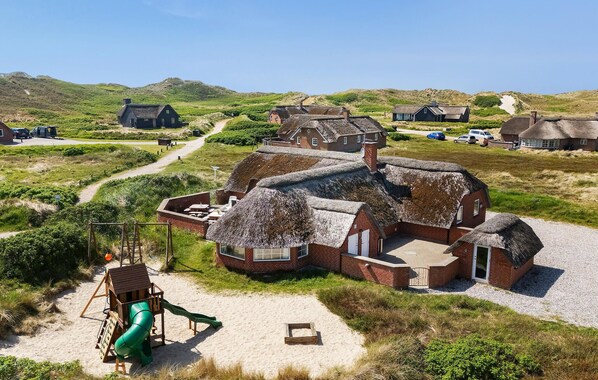 A thatched-roof building with a sandy area and a green slide nearby.