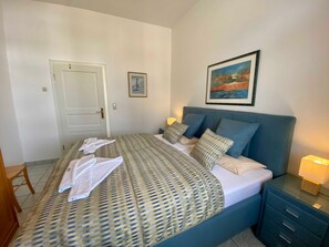 A bedroom with a bed, pillows, a nightstand, a door, and a painting on the wall.