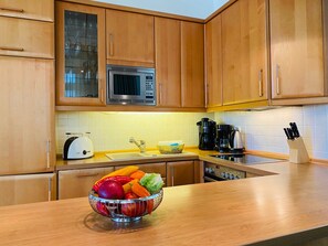 A kitchen with wooden cabinets, a microwave, a toaster, a coffee maker, and a fruit bowl on the counter.