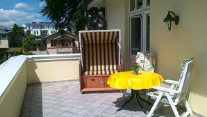 Un balcón con una silla a rayas, una mesita con mantel amarillo y una silla blanca.