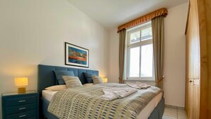 Un dormitorio ordenado con cama, mesitas de noche, ventana con cortinas y un cuadro en la pared.