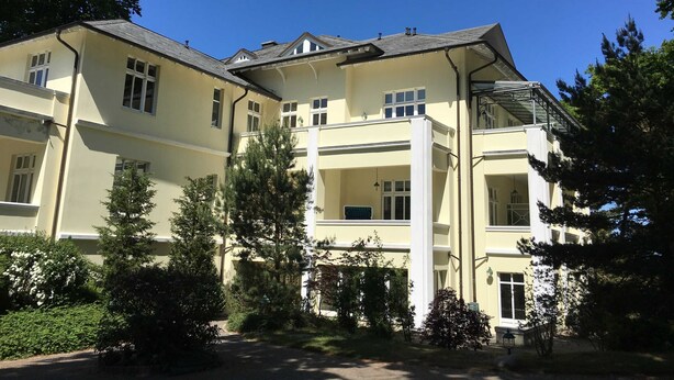Un edificio grande de varios pisos con fachada simétrica, múltiples ventanas y una entrada central.