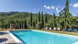 Ein Swimmingpool mit Rutsche, umgeben von Liegestühlen und hohen Bäumen, mit einem Berg im Hintergrund.