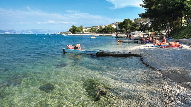 Una spiaggia con acqua cristallina, persone che prendono il sole e imbarcazioni all'orizzonte.