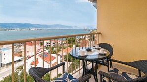 Un balcone con tavolo e sedie, affacciato su una cittadina costiera e il mare.