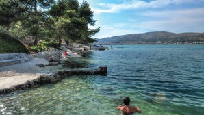 Un lago limpido con una sponda rocciosa, alberi e una città sullo sfondo.