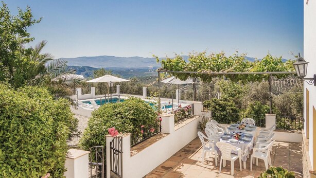 Un área de piscina en la azotea con vistas a montañas distantes, rodeada de exuberante vegetación y mobiliario exterior blanco.