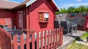 Una casa de madera roja con un porche, una ventana pequeña con cortinas y muebles de exterior.