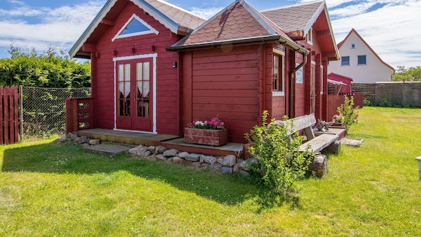 Una casa de madera roja con techo a dos aguas, un porche delantero y un pequeño jardín.
