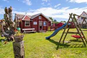 Un bâtiment rouge avec une terrasse en bois, un toboggan bleu et une balançoire en bois.
