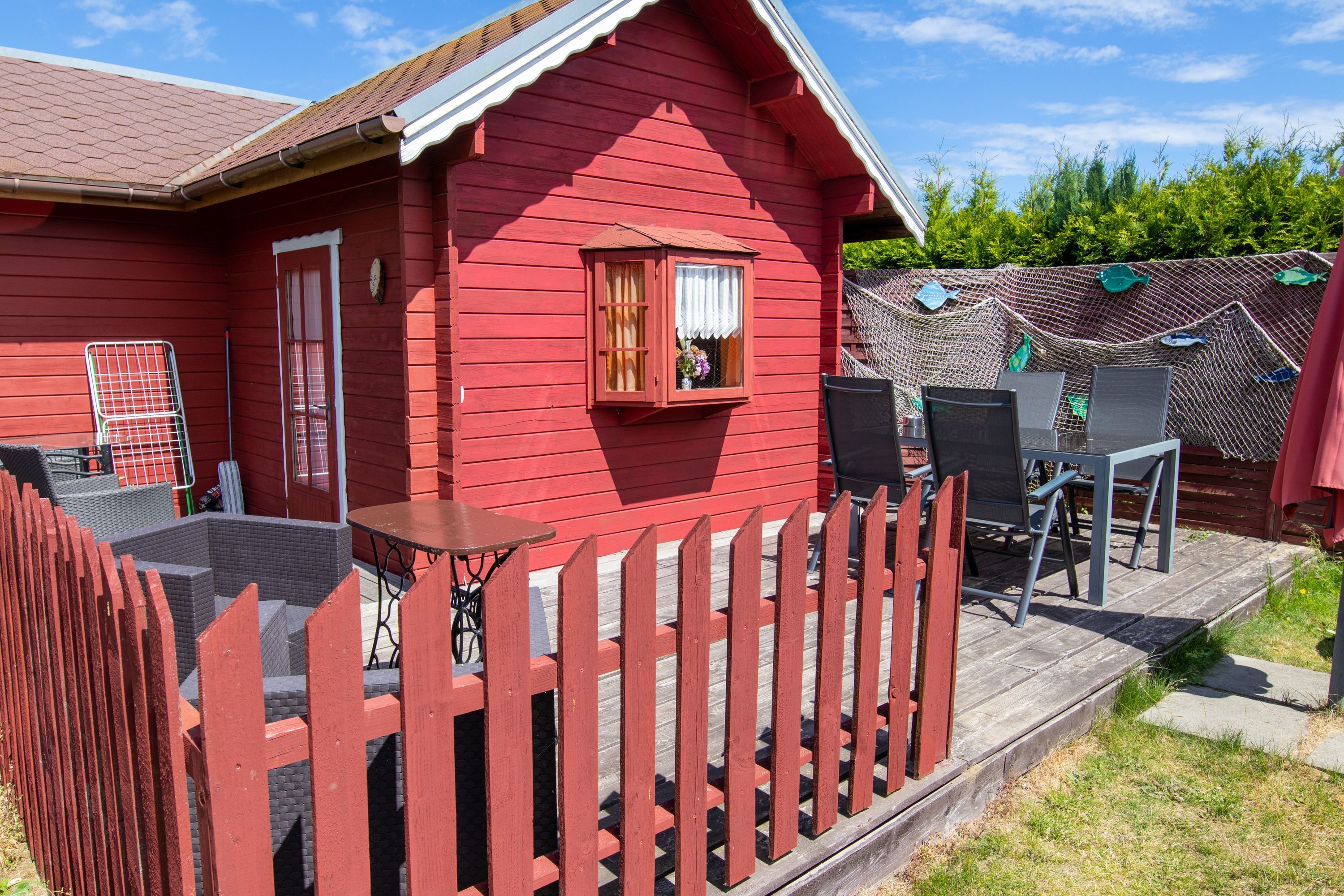 Une maison en bois rouge avec un porche, une petite fenêtre avec des rideaux et du mobilier d’extérieur.
