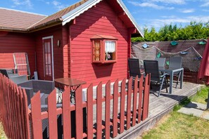Une maison en bois rouge avec un porche, une petite fenêtre avec des rideaux et du mobilier d’extérieur.