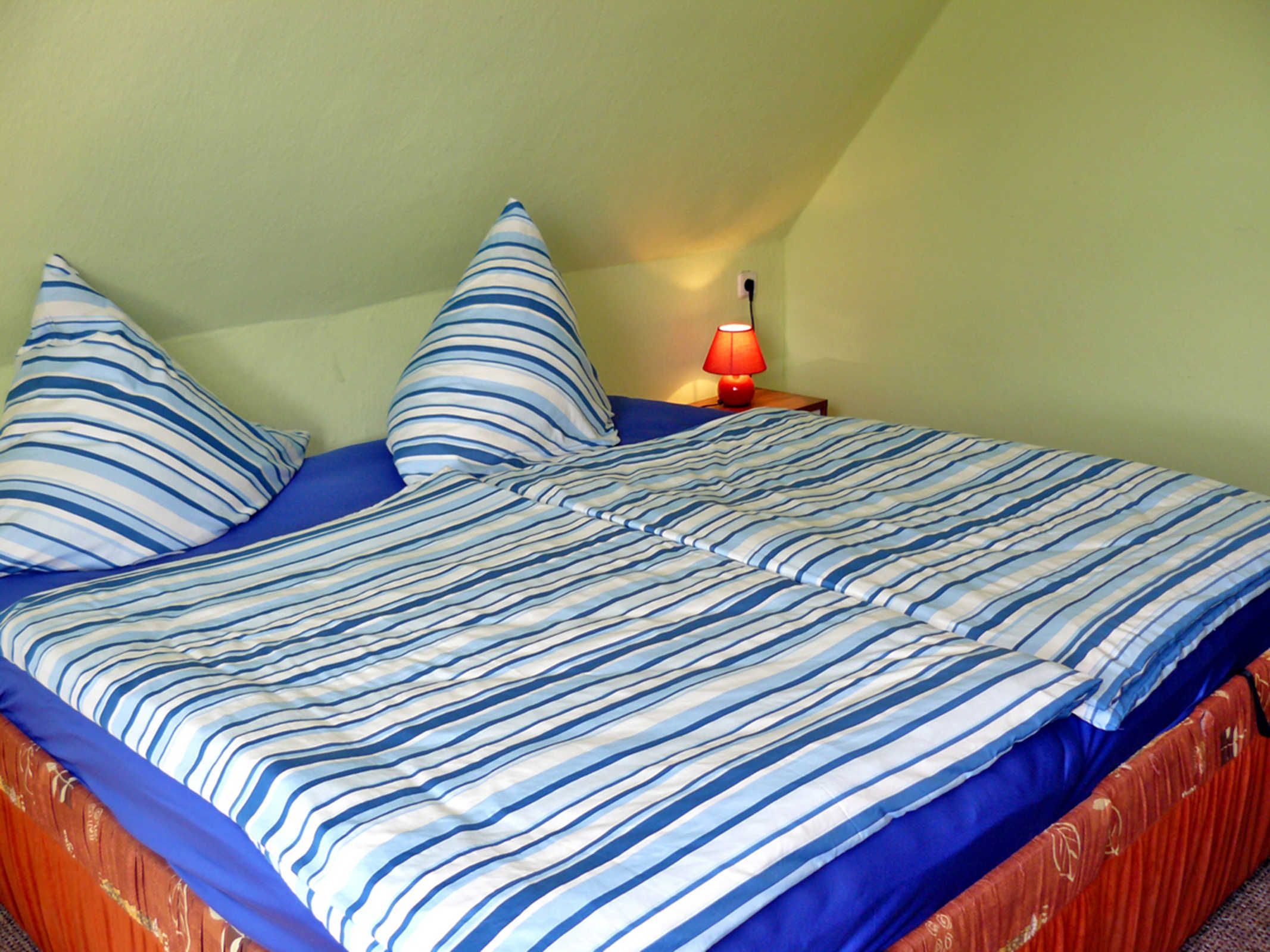 Un lit avec une literie à rayures, une table de chevet avec une lampe et un mur vert.