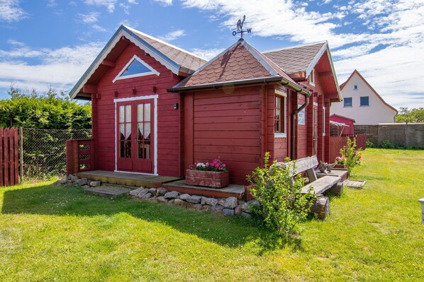A red wooden house with a gabled roof, a front porch, and a small garden area.