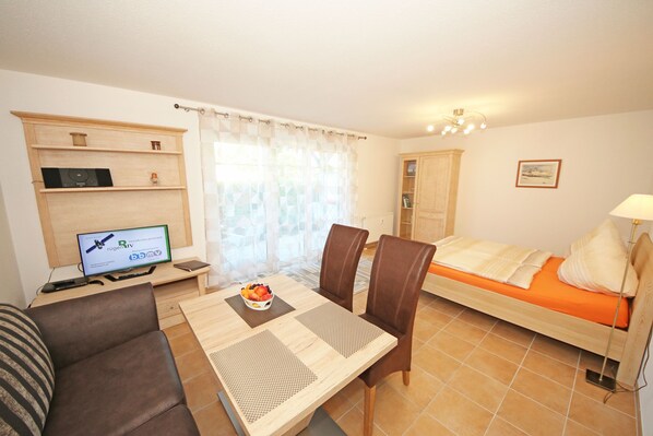 A furnished room with a bed, a desk with a computer, a chair, a sofa, and a window with curtains.