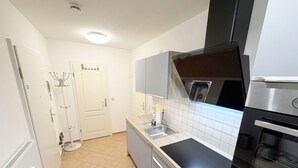 Una cocina compacta con horno integrado, pileta de acero inoxidable y salpicadero de azulejos blancos.