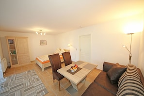 A room with a dining table, chairs, a sofa, a bed, a wardrobe, and a lamp.