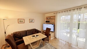 Una sala de estar con un sofá, una mesa de centro de madera, un televisor y un ventanal con cortinas.