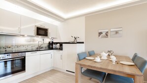 Une cuisine moderne avec des meubles blancs, un four à micro-ondes et une cuisinière. On y trouve une table à manger avec des chaises et un service à thé.