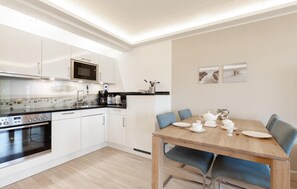 Une cuisine moderne avec des meubles blancs, un four à micro-ondes et une cuisinière. On y trouve une table à manger avec des chaises et un service à thé.