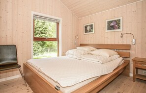 Ein Schlafzimmer mit einem hölzernen Bett, einem Fenster mit Jalousien, einem Nachttisch und zwei gerahmten Bildern an der Wand.