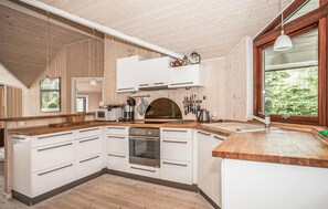 Eine moderne Küche mit Holzschränken, einem eingebauten Ofen und einem großen Fenster mit Blick auf Grünflächen.