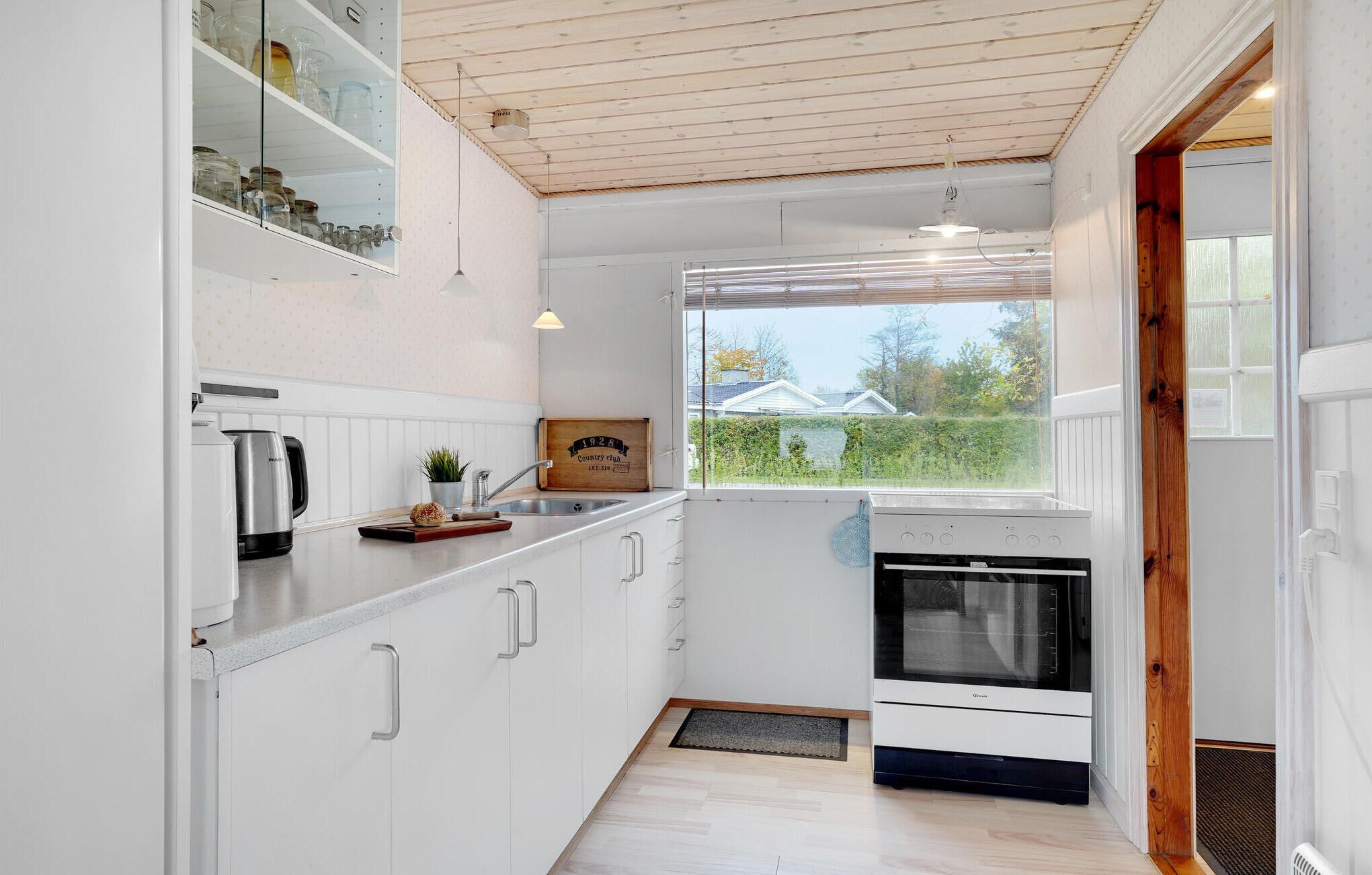 A modern kitchen with white cabinets, a built-in oven, and a window overlooking a garden.