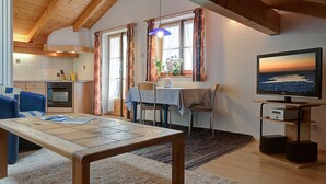 Un accogliente soggiorno con un tavolo in legno, un divano, una TV e una cucina sullo sfondo.