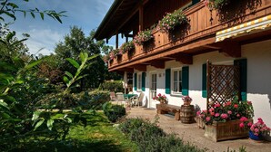 Tipico chalet in legno con un balcone decorato da fiori, immerso nel verde e circondato da un giardino.