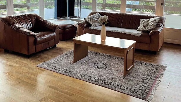 Amplia sala de estar con techo de madera, ventanas grandes, una araña, sofás de cuero y una mesa de centro.