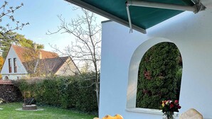 Juego de mesa y sillas de madera al aire libre bajo un toldo verde, con mantel y un jarrón de flores.