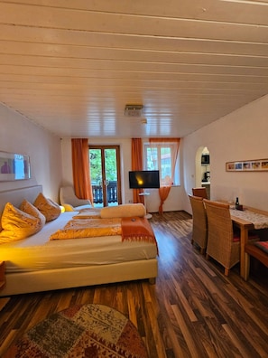 A bedroom with a bed, a television, a dining table with chairs, and a view of the outside.
