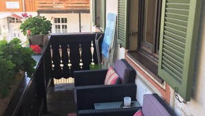 Un balcon avec des meubles en osier, une plante en pot et un bâtiment en bois en arrière-plan.