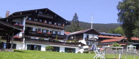 A multi-story building with balconies, a grassy area in front, and a mountain in the background.