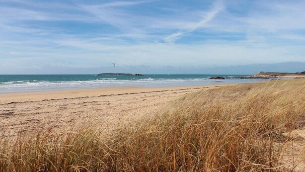 Una platja amb sorra, dunes herboses i un promontori rocosós a la distància.