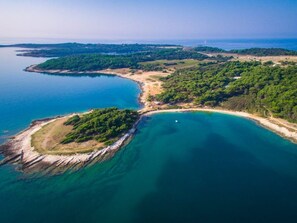 An aerial view of a coastal area with clear blue waters, green vegetation, and a small island.