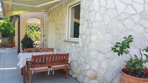 Un bâtiment en pierre avec une table et des chaises sur une terrasse, un pot de fleurs et un petit arbre.