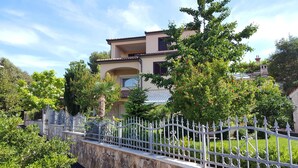 Une maison à deux étages, avec un mur en pierre et une clôture en métal à l’avant.