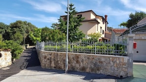 A residential street with a stone wall, a metal fence, and houses with tiled roofs.