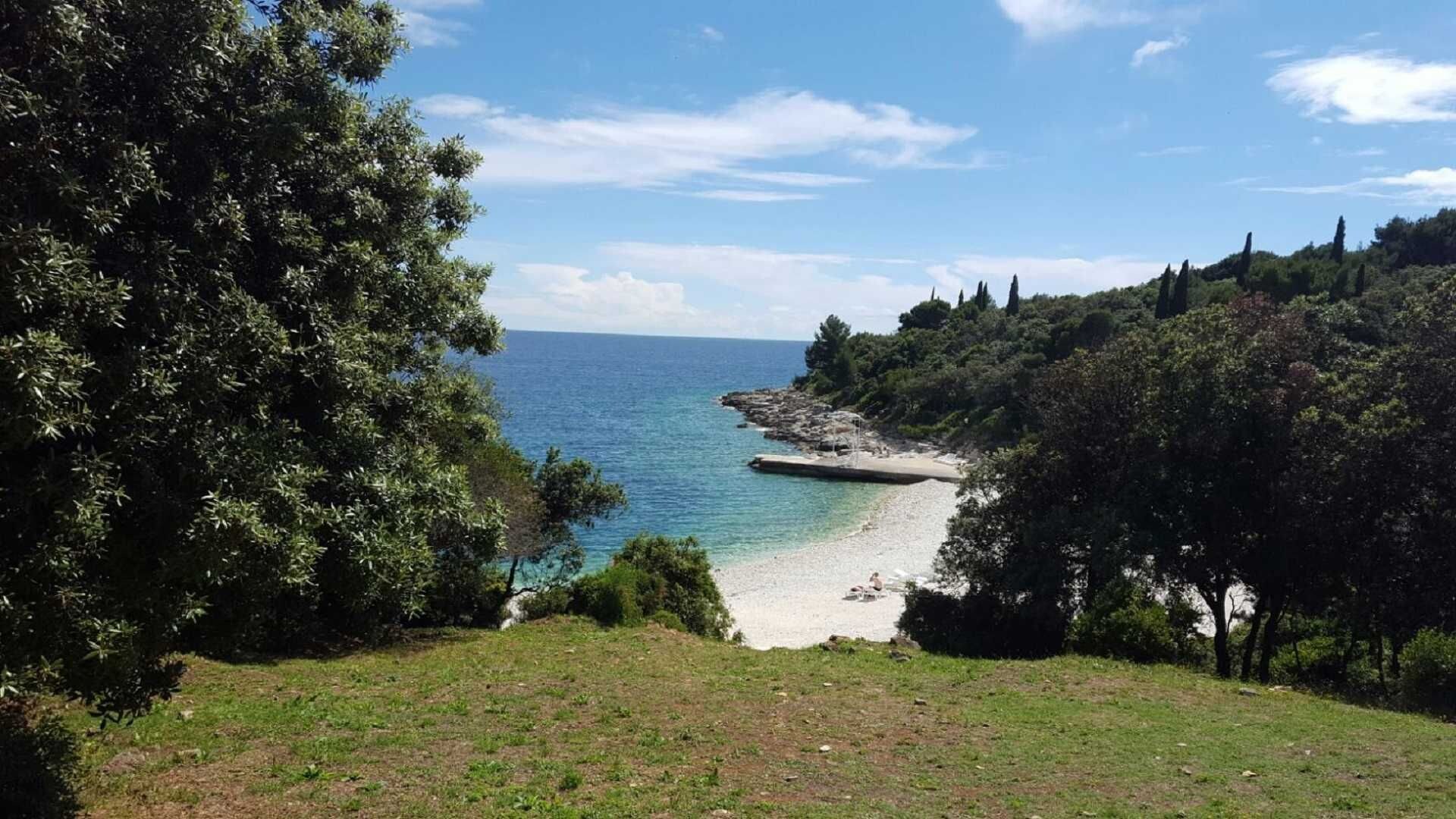 Ett kustlandskap med fri utsikt över havet, en sandstrand och omgivande grönska.