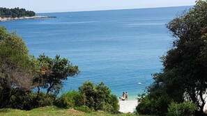 Uitzicht op de kust met helderblauw water, bomen en een zandstrand.