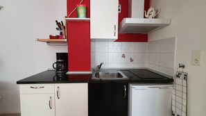 Een keuken met een zwart aanrecht, witte kasten, een witte koelkast, een koffiezetapparaat en een rode muur.