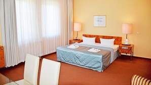 Una habitación de hotel con una cama, dos mesitas de noche, una silla, una mesita de cristal y una cortina.