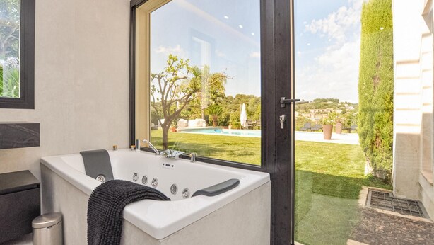 A modern bathroom with a large bathtub, a window overlooking a pool and garden. - Stunning home in Biot (Biot)