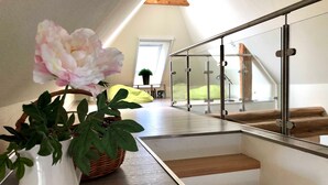 Un interior moderno con una escalera, un jarrón blanco con una flor y un sillón informal verde.